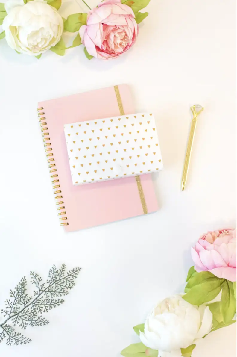 This image shows a diary with a gold pen. It also shows some flowers scattered around.