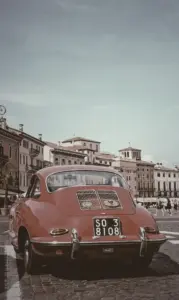 Red car against old buildings in Verona city, Italy, with CSS saturate filter set to 20%, resulting in a more grayish appearance compared to the original photo.