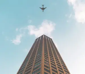 This image displays a photo of a brown building with the sky in the background and an airplane flying overhead.