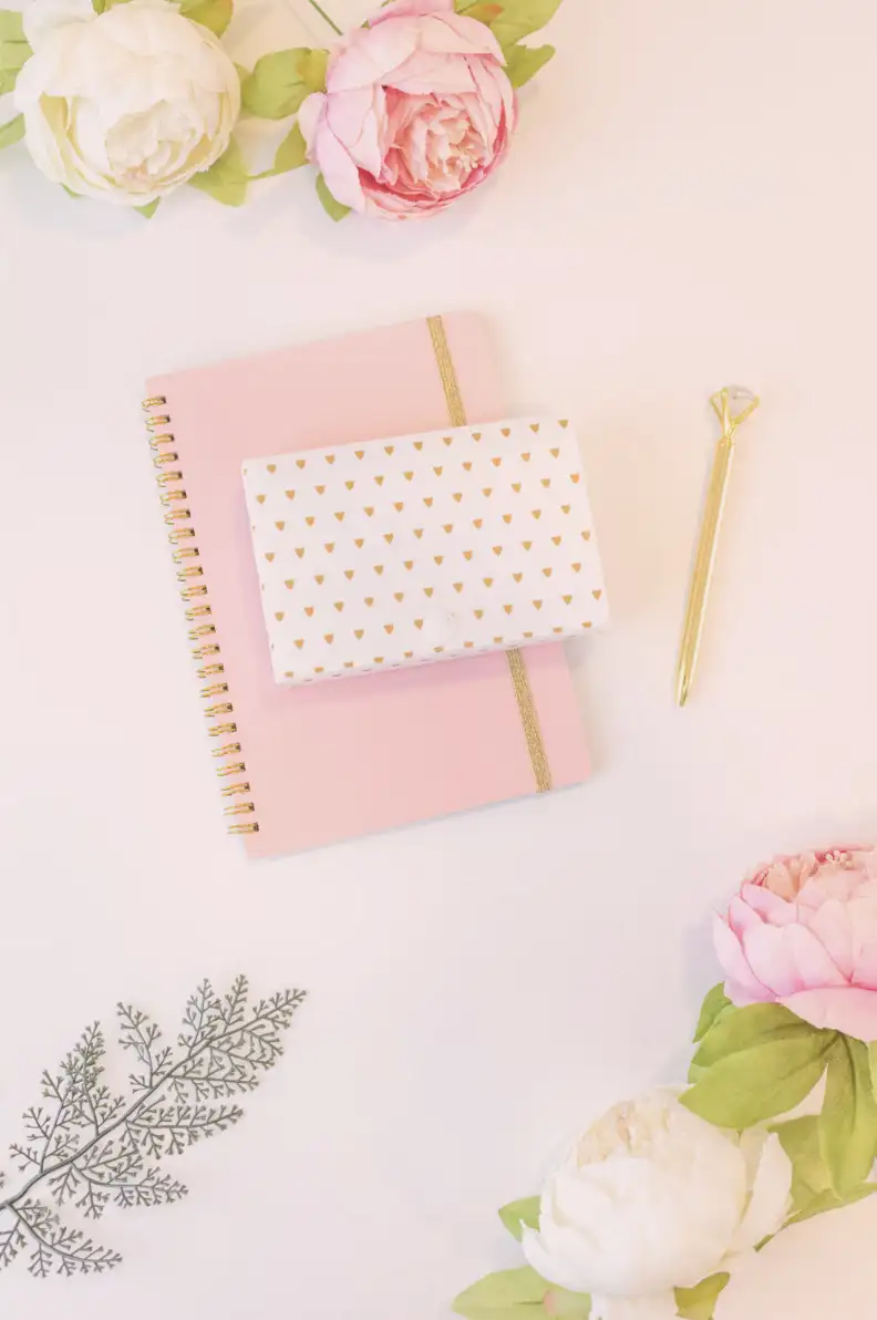 Utilizing the css overlay effect. This image shows a diary with a gold pen. It also shows some flowers scattered around. We set the background-color: rgba(220, 135, 135, 0.2); and we add a pale pink color with a slight see-through effect.