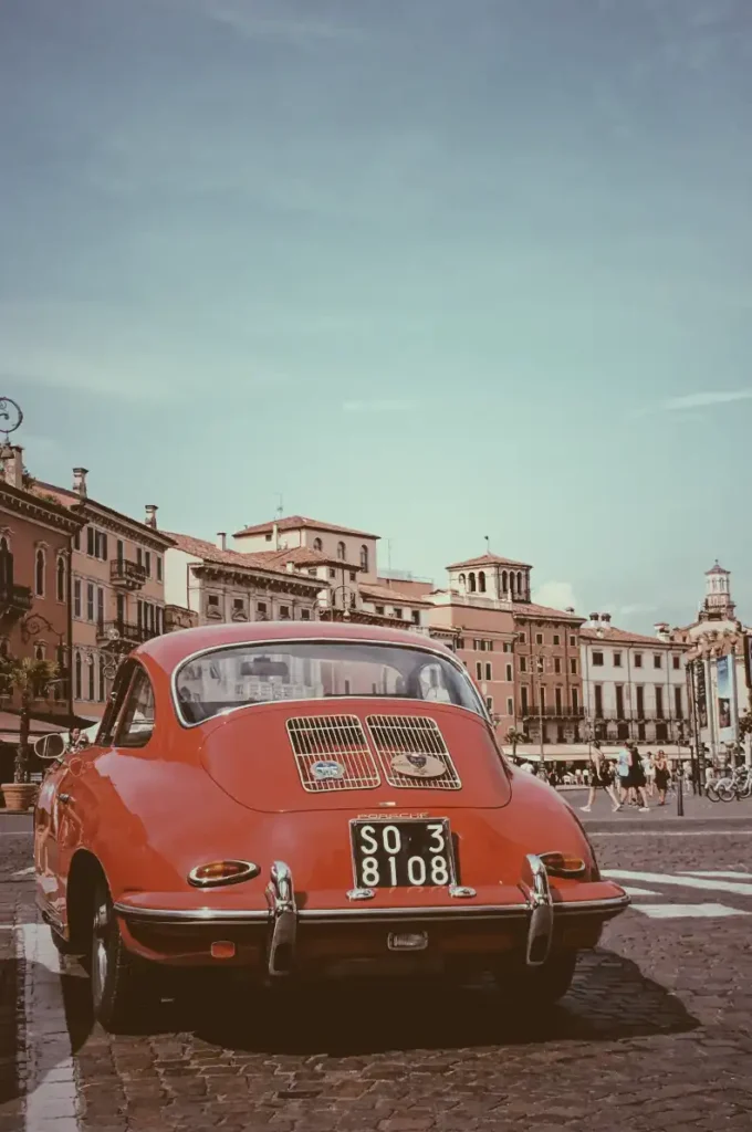 This image shows a photo of a red car with old buildings as a background.This photo was captured in Verona city Italy.
