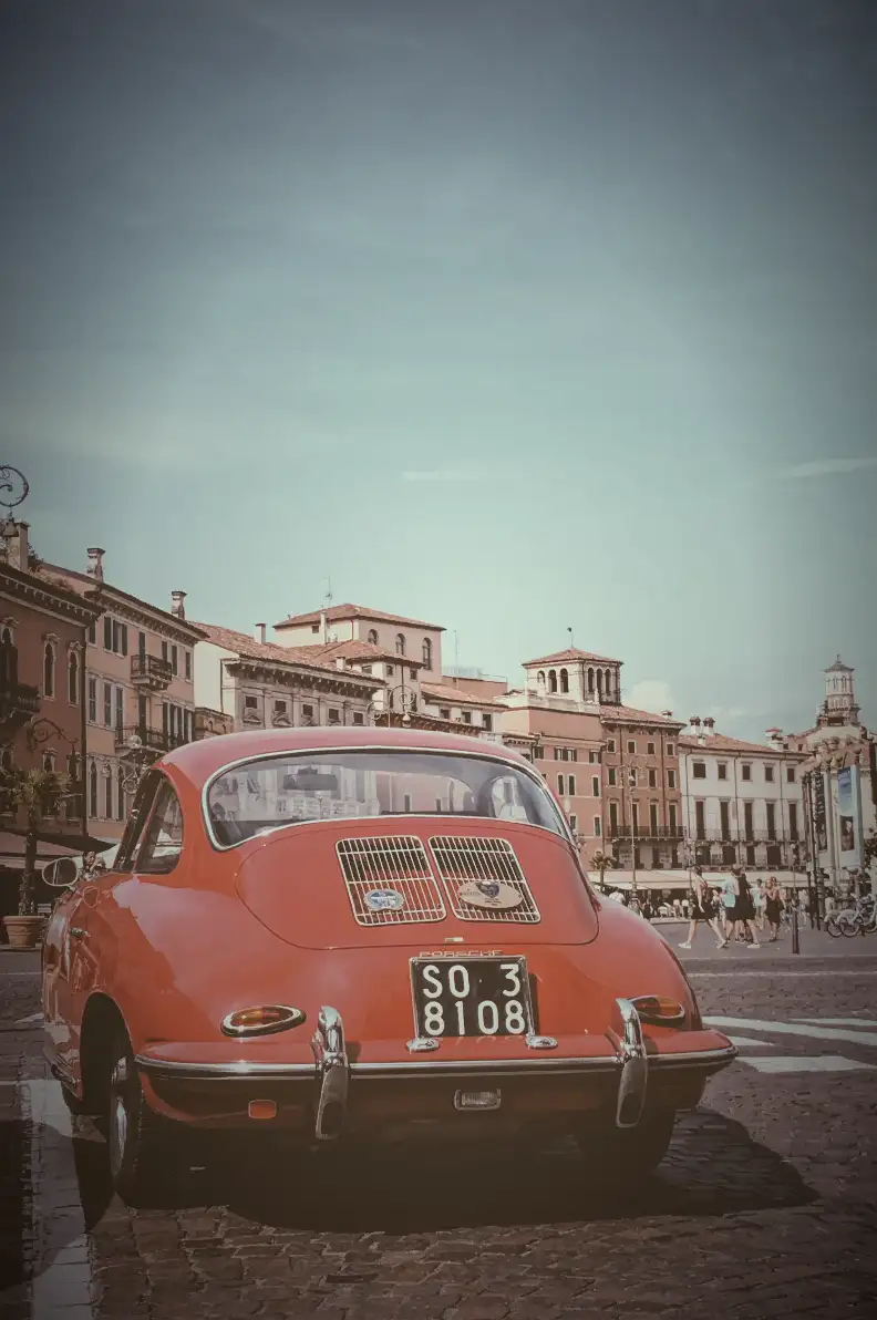 Utilizing the radial-gradient overlay. This image shows a photo of a red car with old buildings as a background.This photo was captured in Verona city Italy. We set the background-image: radial-gradient(
rgba(255, 255, 255, 0.1),
rgba(128, 128, 128, 0.2),
rgba(0, 0, 0, 0.6)
); and it creates a unique overlay effect using a circular pattern. It transitions from shades of light gray to dark gray.