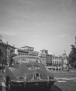Utilizing the grayscale filter. This image shows a photo of a red car with old buildings as a background.This photo was captured in Verona city Italy. We set the css filter: grayscale(100%).